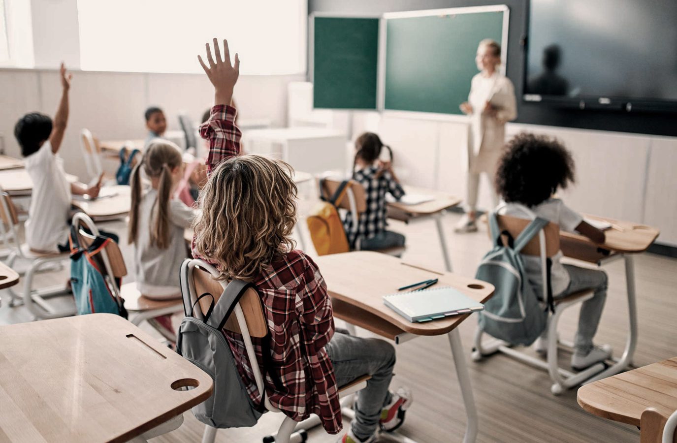 a classroom with children sitting at desks and raising their hands at The parcHAUS at Firewheel Parkway